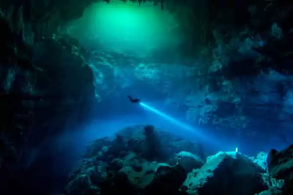 Buzo atravesando las aguas del cenote con ua lámpara