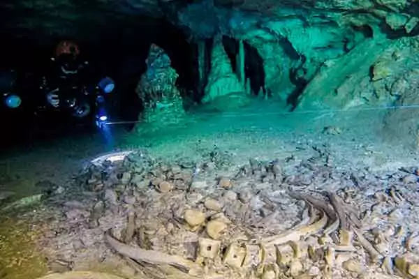 Buzo explorando las profundidades de un cenote con ofrendas mayas