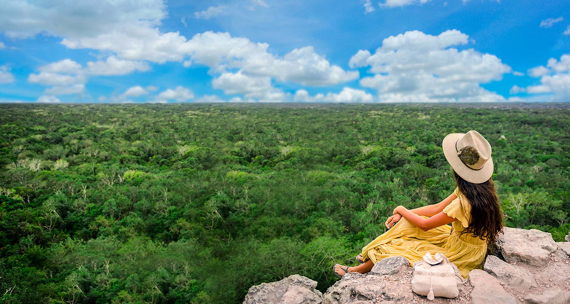 Mujer joven con vestido amarillo sentada en la cima de Coba mirando al horizonte de la jungla maya