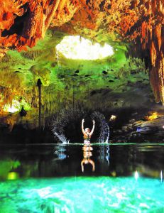 Mujer joven saliendo del agua de un cenote semiabierto