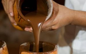 Mujer vaciando chocolate natural liquido de un jarrón de barro.